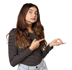 Young Caucasian woman in studio setting shocked pointing with index fingers to a copy space.