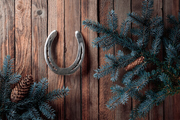 Old horseshoe and blue spruce branches with cones on a old wooden background.