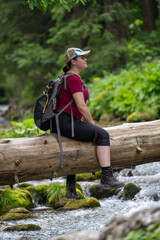 a break in a mountain hike, sitting on a log that has fallen over a stream, a woman looks around