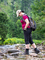 Fototapeta na wymiar on a mountain hike, a woman stops by a stream and looks around