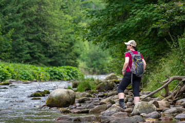 on a mountain hike, a woman stops by a stream and looks around
