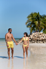 Young couple on vacation walking on the beach with no one around, surrounded by palm trees in Holbox, Mexico.