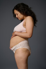 new mon in underwear, shows her postpartum belly with stretch marks and flaws, isolated gray. Post...