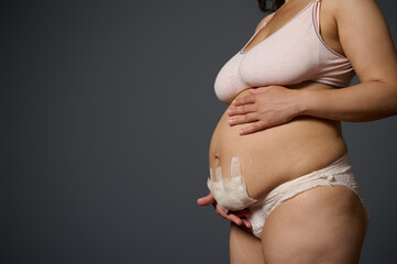 Close-up naked postpartum belly with bandage after cesarean C-section of a body positive woman mother, isolated on gray - obrazy, fototapety, plakaty