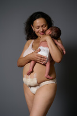 Happy mother smiling while holding her newborn baby and showing naked belly with bandage hiding...