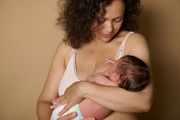 Close-up happy woman, loving caring happy mother smiles looking at her newborn baby, she holds in arms, beige background - obrazy, fototapety, plakaty