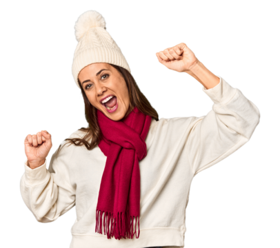Middle-aged woman in cozy Christmas winter wear in studio raising fist after a victory, winner concept.