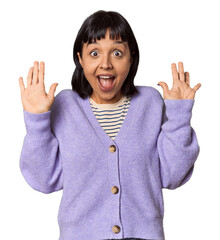 Young Hispanic woman with short black hair in studio receiving a pleasant surprise, excited and...