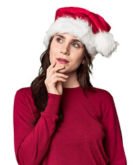 Young woman in Santa hat and red sweater looking sideways with doubtful and skeptical expression.