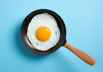A fried egg in a frying pan on a blue background - obrazy, fototapety, plakaty