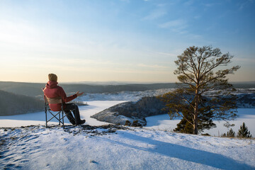 Male person meditation winter nature day. Man  sitting in chair  meditating on top of the mountain during cold fogy morning sunrise