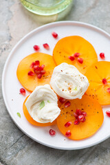Persimmon slices with torn mozzarella and pomegranate seeds on a white plate, middle close-up, vertical shot, selective focus
