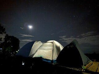 Camping under the moonlight, with a tent pitched and a campfire glowing in the middle of the night.