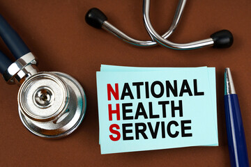 On a brown surface there is a stethoscope, a pen and blue stickers with the inscription - National Health Service - Powered by Adobe
