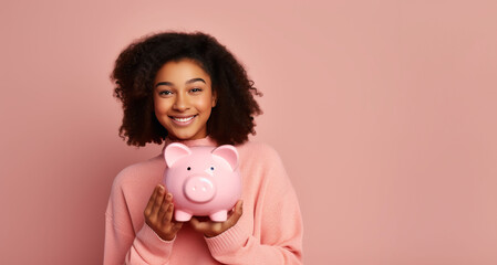 Fototapeta na wymiar Joyful young woman with curly hair holding a piggy bank on a pink backdrop