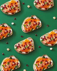Pattern of toasts with cream cheese, persimmon and pomegranate seeds on green background. Creative...