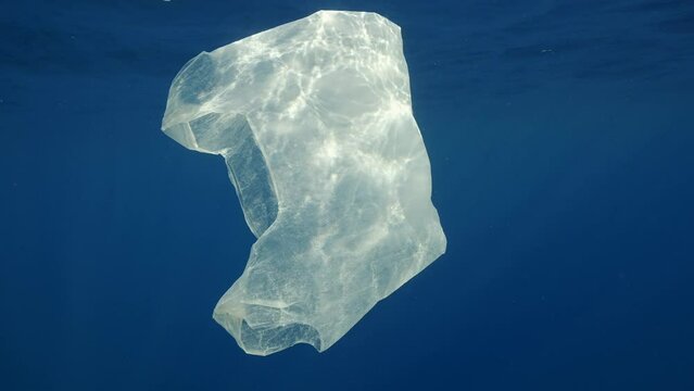 Close uo of discarded disposable white plastic bag slowly swims under waves of Mediterranean sea in bright sunbeams, Slow motion. Plastic pollution of Ocean