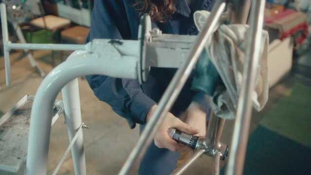 Mechanic in blue workwear coat repairing bicycle with crank puller tool in the workshop