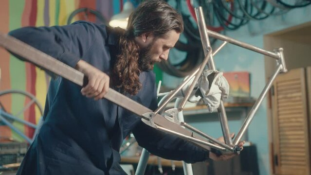 Mechanic working with hand tool and carrying out repairs on bike frame held by workstand in the workshop