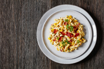 mac and cheese with corn, bacon topped with panko breadcrumbs on plate on dark wooden table, horizontal view from above, flat lay, free space