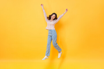 Fototapeta na wymiar Cheerful Asian woman in casual clothes smiling and jumping with hands up in colorful yellow color isolated background studio shot