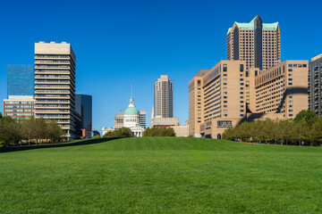 Fototapeta na wymiar View across green lawn of Gateway Arch National Park with other office buildings in downtown cityscape