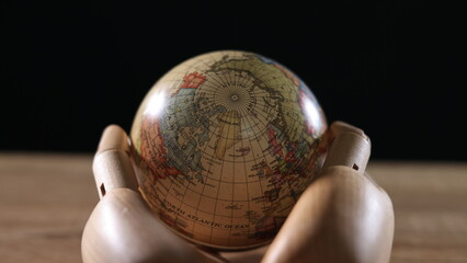 On a black background, a wooden model hand holds the Earth, symbolizing the importance of...