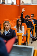 Student raising hand while attending a lecture with his classmates