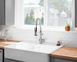 A kitchen sink detail with a butcher block wood countertop, white subway tile backsplash, grey...