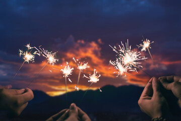 A joyful group of youths enjoying a game of sparklers on a mountain during the summer dusk.  While...