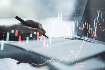 Multi exposure of abstract creative financial graph with world map and with hand writing in notebook on background with laptop, forex and investment concept
