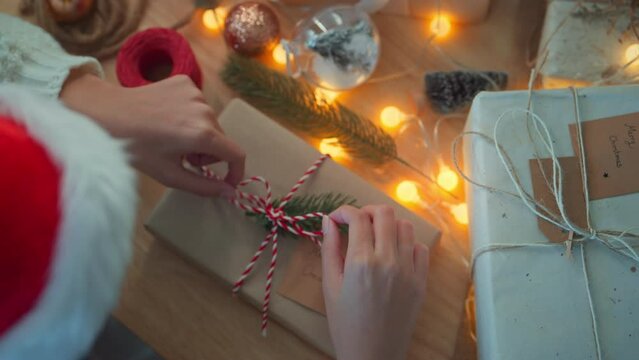Top view - Woman decorates a box wrapped in crab paper with a fir branch, Female hands decorating Christmas present, Christmas gifts wrapping