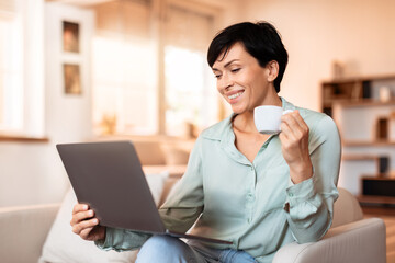 lady browsing laptop for online work holding coffee at home