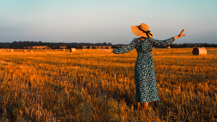 girl on a mown field in a hat and blue dress with her back