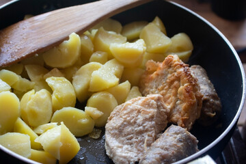 Fried yellow potato with meat in a black pan