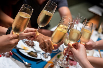 A group of people raise a toast with glasses of Prosecco or sparkling wine on the table - obrazy, fototapety, plakaty