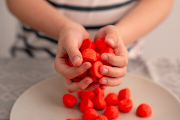 Sweet indulgence in the hands of a child red fruity candies on a plate, a testament to the...