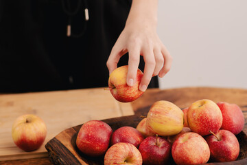 Female hands arrange a selection of ripe red apples on a wooden board, symbolizing the nourishing...