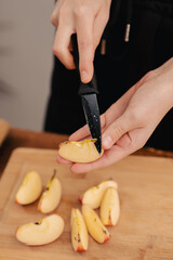 Fruitful preparation: A woman's hands expertly cut through a red apple on a wooden chopping board, embodying the essence of healthy eating, vegetarian values, and the nutritional advantages of fruit