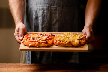 Rustic Pizza Moment: A snapshot of male hands showcasing two small homemade pizzas on a wooden board