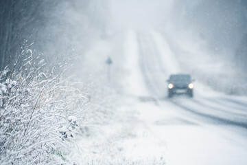 The car is driving on a winter road in a blizzard. Focus on foreground