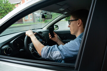 Male driver sits in a car and looks at a smartphone screen