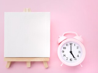 Wooden easel with empty blank Canvas and Pink alarm clock at 5am 5pm