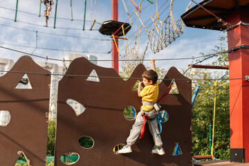 A happy child, a healthy boy is enjoying a summer day in a climbing adventure park. Overcoming obstacles