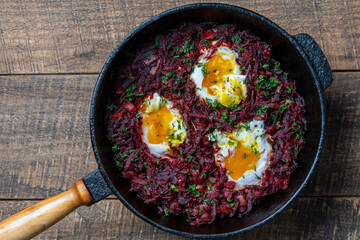 Boiled red beets with fried eggs, red peppers, onions and green dill in a frying pan on a wooden table, closeup, top view. Food background. Healthy food