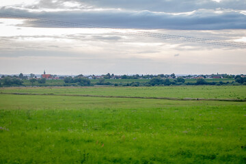 Green farm meadows and a European village in the distance on the horizon. European rural landscape in the evening