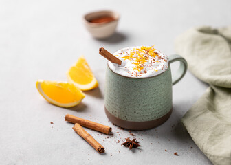 Mug of hot chocolate with whipped cream, orange zest and cinnamon sticks on a light gray background