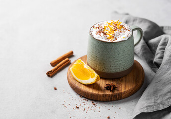 Mug of hot chocolate with whipped cream and orange zest on a wooden board on a light  background...