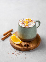 Mug of hot chocolate with whipped cream and orange zest on a wooden board on a light  background with a cinnamon sticks and fresh orange slices.