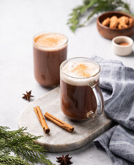 Two glass mugs with hot chocolate and milk foam on a light marble board on a gray background